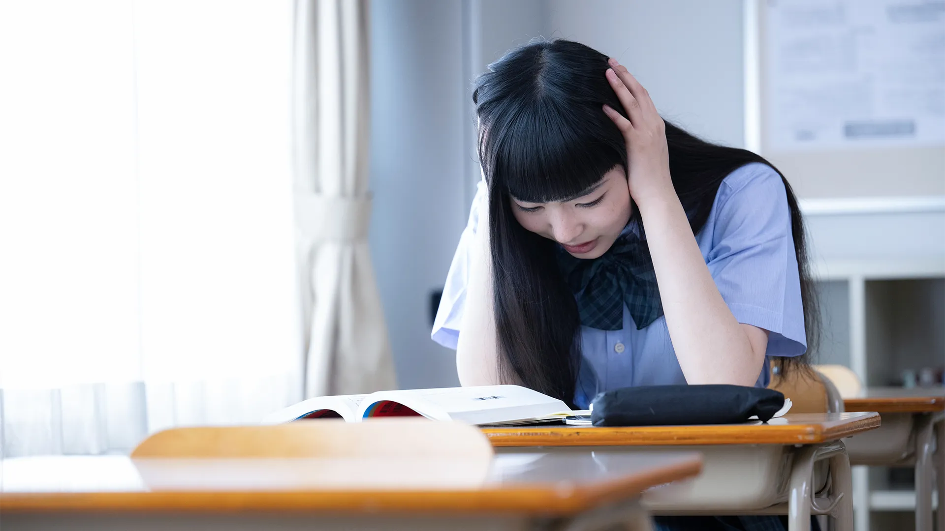 参考書を前に、大学受験の難しい課題に直面し、深く考え込んでいる高校生
