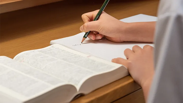 集中できる環境づくりの大切さを示す画像。シンプルな机の上で、生徒が参考書を開き、ノートに鉛筆で書き込んでいる手元が写っている。