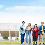 大学キャンパスの屋外で資料を持つ学生が並ぶ